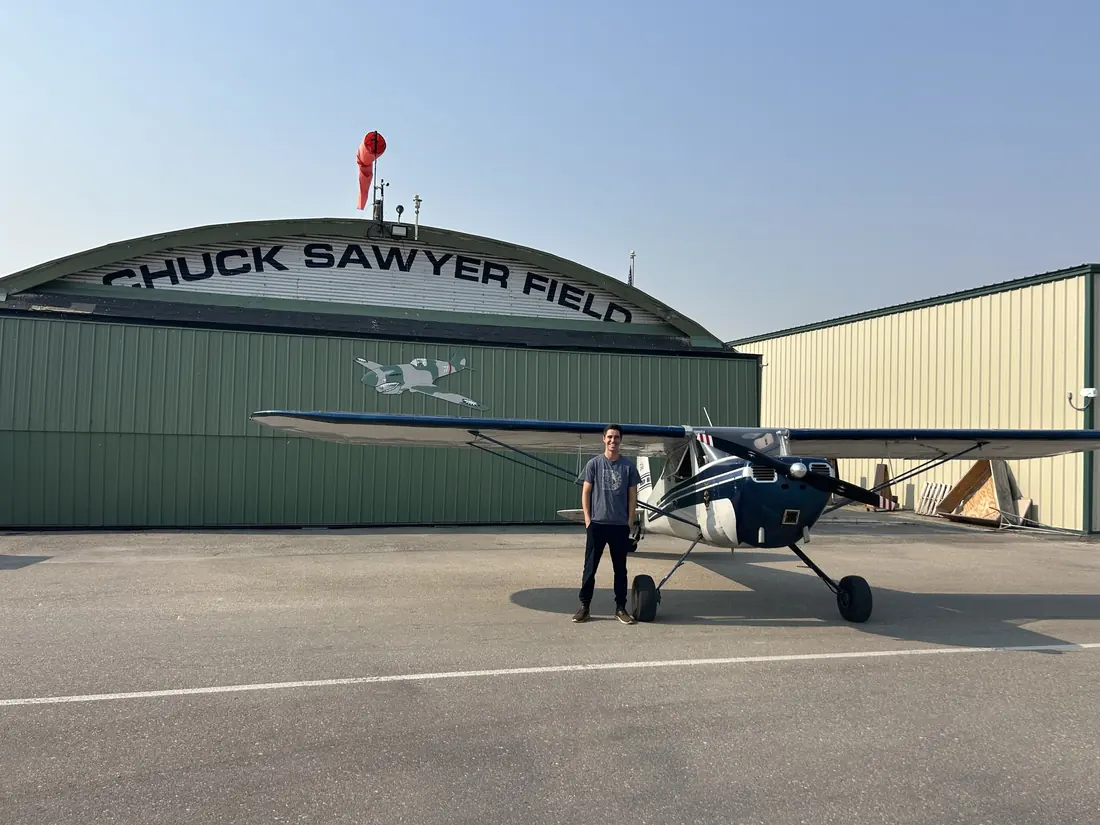 Student pilot standing with Cessna 140 N2353V in front of the Chuck Sawyer Field hangar