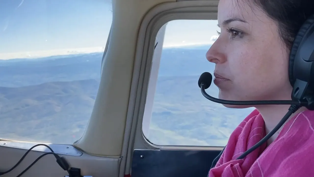 A student pilot at the controls of a Cessna 172, foothills visible through the cockpit window